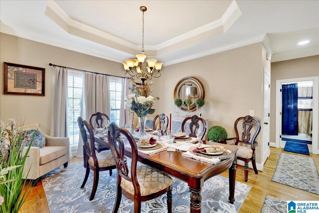 dining area with a raised ceiling, crown molding, light hardwood / wood-style flooring, and a chandelier