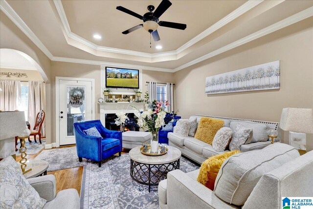 living room featuring ceiling fan, wood-type flooring, ornamental molding, and a tray ceiling