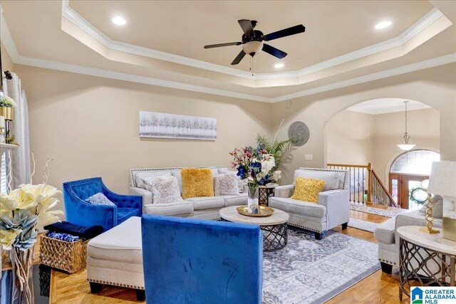 living room featuring wood-type flooring, a raised ceiling, and crown molding