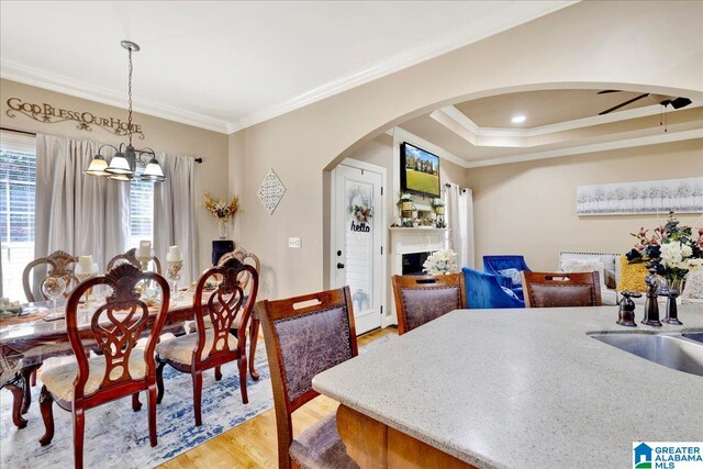 dining room featuring ceiling fan with notable chandelier, light wood-type flooring, a tray ceiling, and ornamental molding