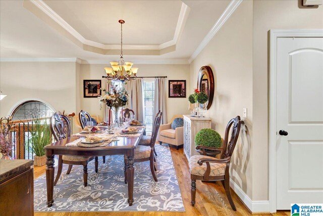 dining space with a tray ceiling, an inviting chandelier, ornamental molding, and light wood-type flooring