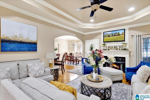 living room featuring a tray ceiling, crown molding, ceiling fan with notable chandelier, and hardwood / wood-style flooring