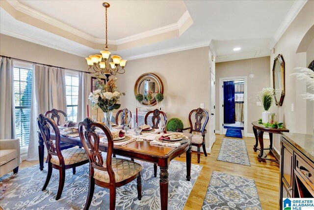 dining space with a notable chandelier, light wood-type flooring, ornamental molding, and a tray ceiling