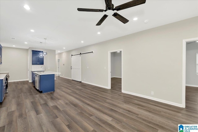 unfurnished living room with sink, dark wood-type flooring, a barn door, and ceiling fan