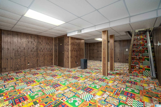 basement featuring a drop ceiling and wood walls