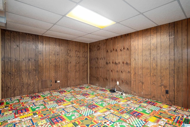 unfurnished bedroom featuring a drop ceiling and wooden walls