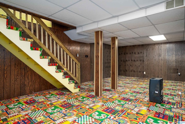 basement with a drop ceiling and wood walls