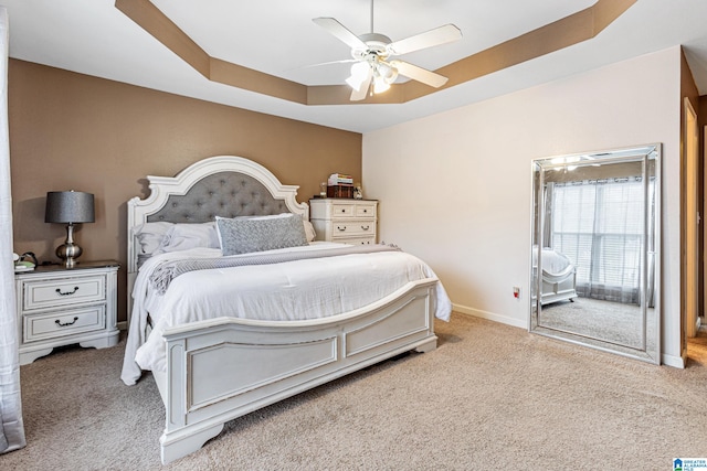 carpeted bedroom with a raised ceiling and ceiling fan