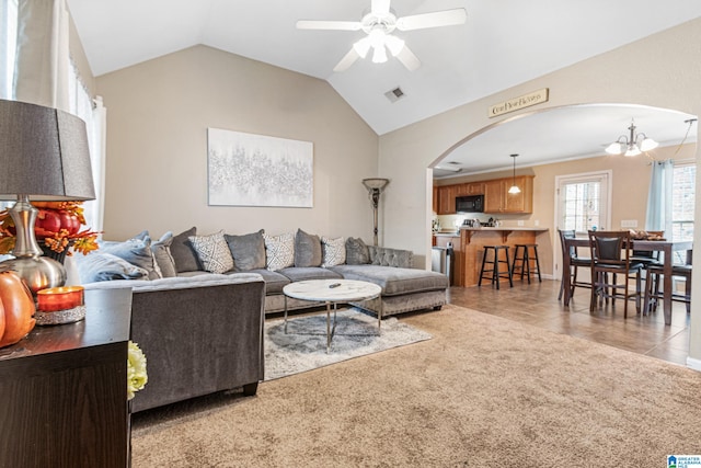 carpeted living room featuring ceiling fan with notable chandelier and vaulted ceiling