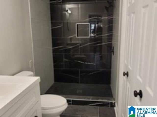 bathroom featuring a tile shower, vanity, and toilet