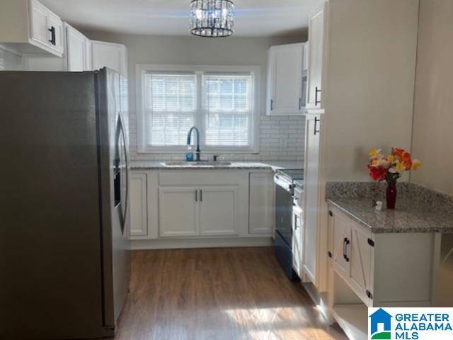 kitchen with white cabinets, black electric range oven, sink, and stainless steel refrigerator