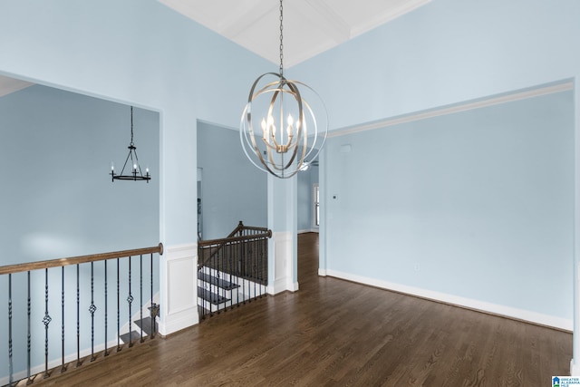 unfurnished dining area featuring a towering ceiling, dark hardwood / wood-style floors, an inviting chandelier, and crown molding