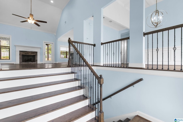 stairs with wood-type flooring, ceiling fan with notable chandelier, high vaulted ceiling, and ornamental molding