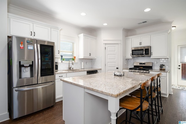 kitchen featuring appliances with stainless steel finishes, dark hardwood / wood-style flooring, ornamental molding, white cabinets, and a center island