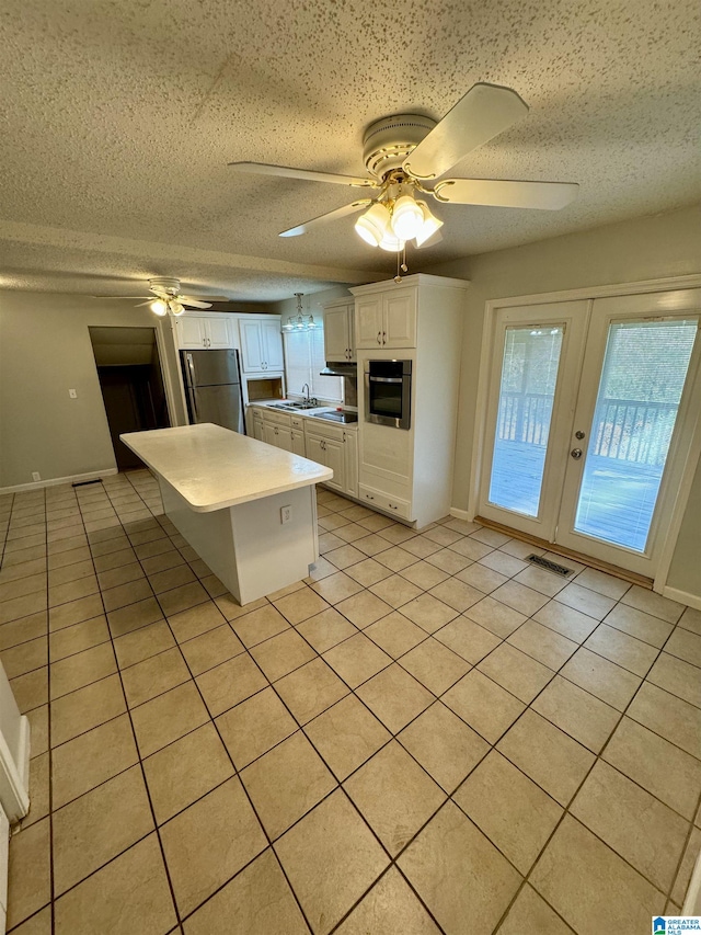 kitchen featuring appliances with stainless steel finishes, a textured ceiling, ceiling fan, light tile patterned floors, and white cabinets