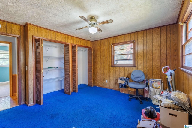 unfurnished office featuring a textured ceiling, dark carpet, ceiling fan, and wood walls