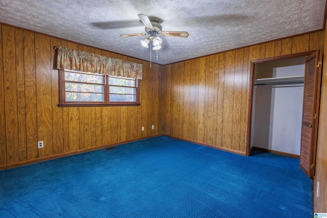 unfurnished bedroom with a textured ceiling, a closet, ceiling fan, and wood walls