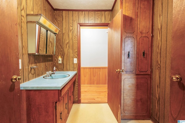 bathroom featuring vanity, crown molding, a textured ceiling, and wooden walls