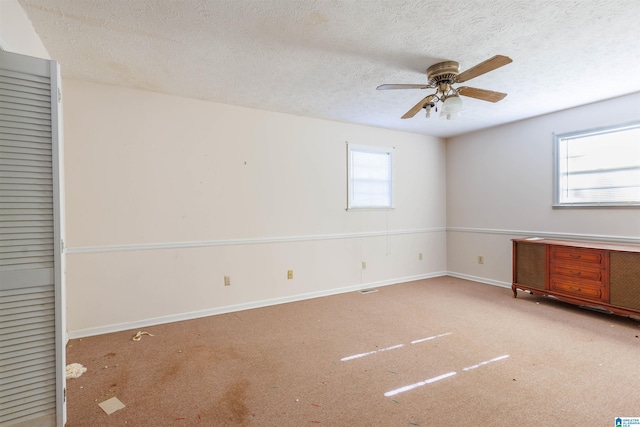 carpeted empty room featuring ceiling fan, a healthy amount of sunlight, and a textured ceiling