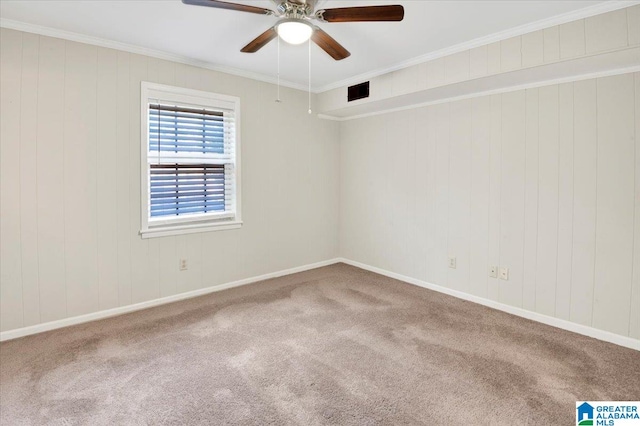 carpeted empty room with ceiling fan, wood walls, and ornamental molding