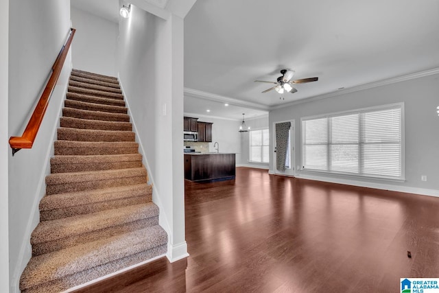 stairway with ceiling fan, sink, wood-type flooring, and crown molding