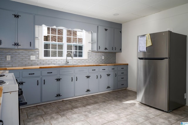 kitchen with white range oven, butcher block counters, stainless steel fridge, and tasteful backsplash