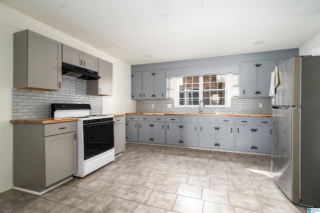 kitchen featuring gray cabinetry, wooden counters, stainless steel fridge, tasteful backsplash, and white gas stove