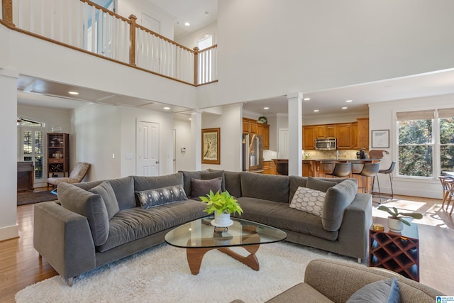 living room featuring ornate columns, crown molding, light hardwood / wood-style flooring, and a high ceiling