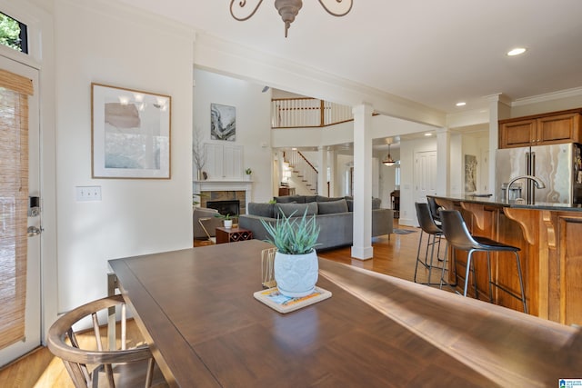 dining area featuring light wood-type flooring, crown molding, and a tiled fireplace