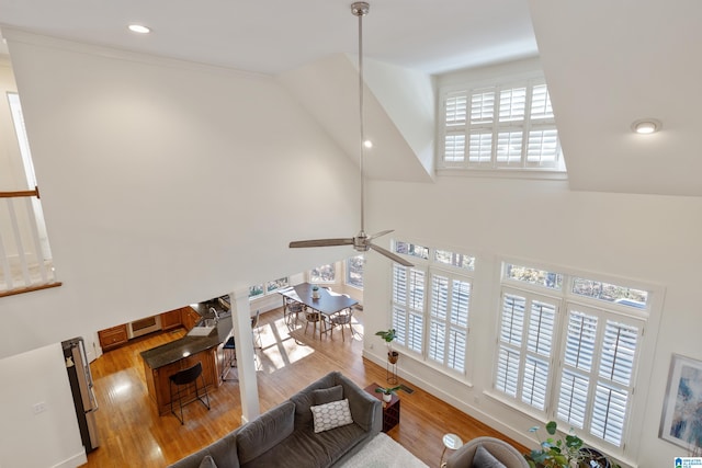 living room with light wood-type flooring, a towering ceiling, and ceiling fan