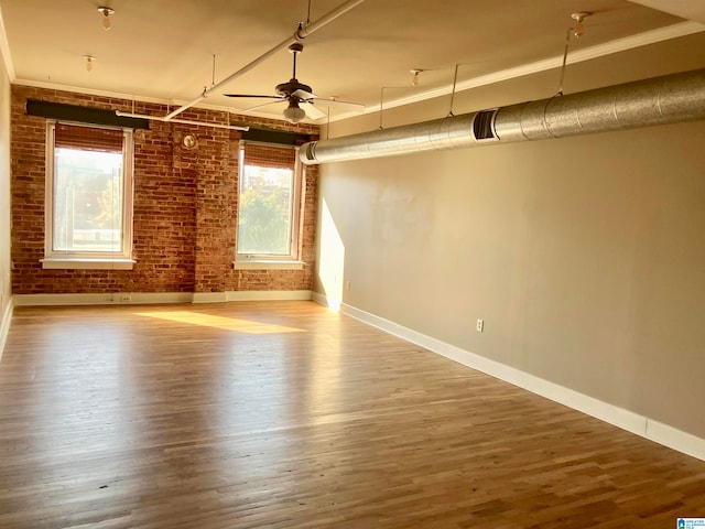 empty room with ceiling fan, brick wall, and wood-type flooring