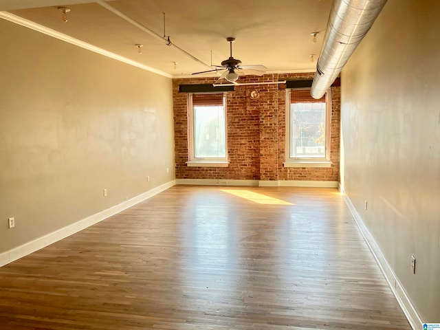 empty room with hardwood / wood-style flooring, ceiling fan, brick wall, and ornamental molding