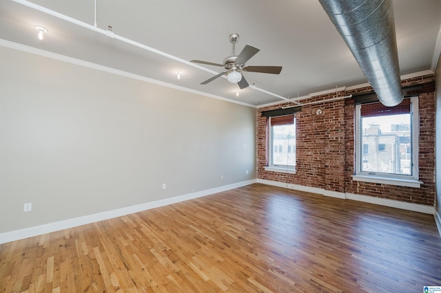 unfurnished room featuring hardwood / wood-style flooring, ceiling fan, ornamental molding, and brick wall