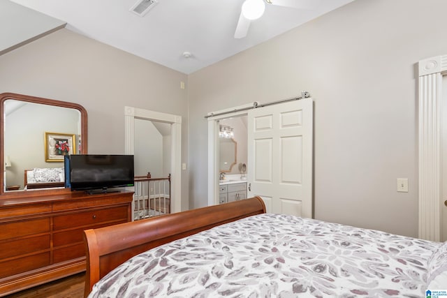 bedroom with a barn door, ensuite bathroom, and ceiling fan