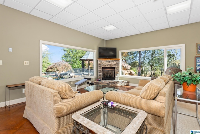 tiled living room featuring a stone fireplace, a wealth of natural light, and a paneled ceiling