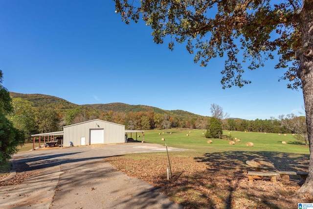 view of yard featuring a rural view, an outdoor structure, a garage, a mountain view, and a carport