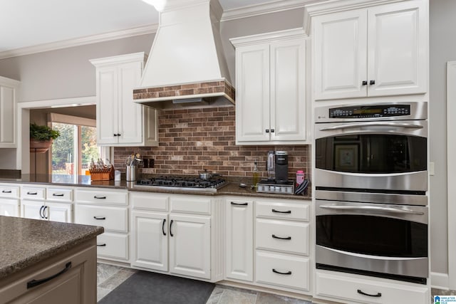 kitchen with decorative backsplash, ornamental molding, custom range hood, stainless steel appliances, and white cabinets