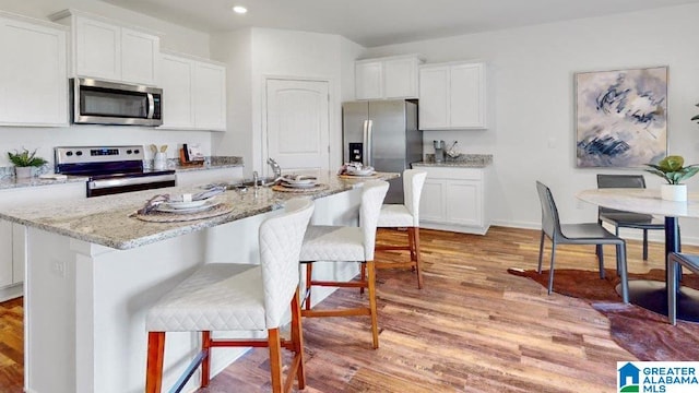 kitchen with white cabinets, a kitchen breakfast bar, a center island with sink, light hardwood / wood-style flooring, and appliances with stainless steel finishes