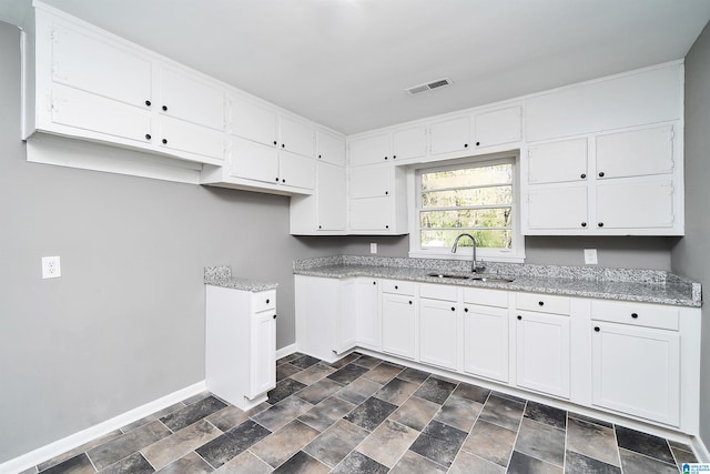 kitchen with white cabinets, light stone countertops, and sink