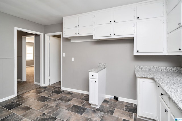 kitchen featuring light stone countertops and white cabinetry