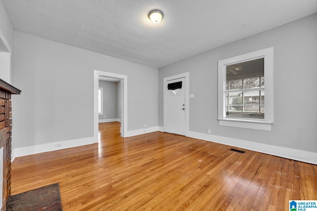 unfurnished living room featuring hardwood / wood-style floors, a textured ceiling, and a brick fireplace