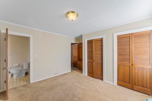 unfurnished bedroom featuring a textured ceiling, ensuite bathroom, light carpet, and two closets