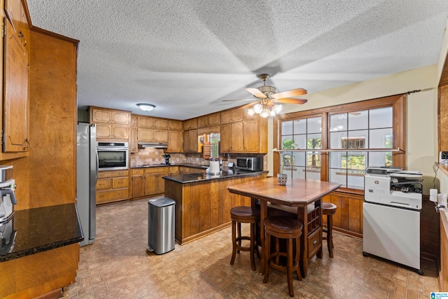 kitchen with tasteful backsplash, a breakfast bar, a textured ceiling, stainless steel appliances, and ceiling fan