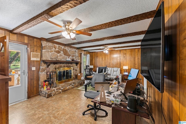 office space with beam ceiling, a stone fireplace, a textured ceiling, and wooden walls