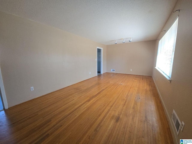 empty room featuring a textured ceiling, wood finished floors, visible vents, and baseboards