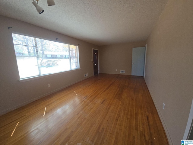 unfurnished room with visible vents, a textured ceiling, baseboards, and wood finished floors