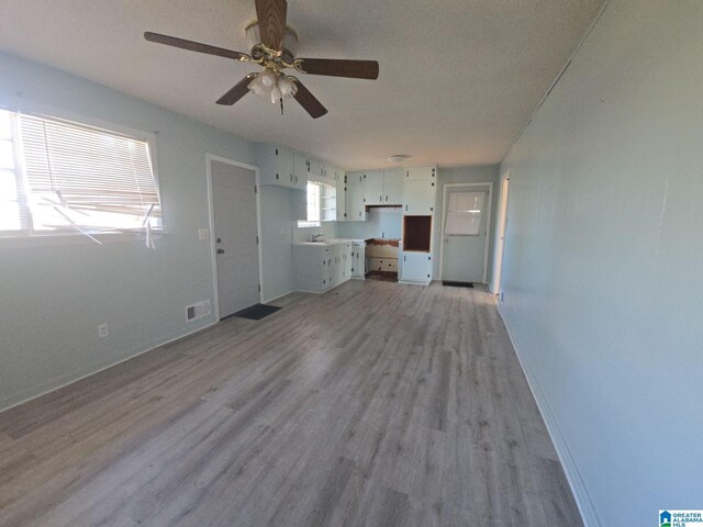 unfurnished living room featuring light wood-style flooring, a sink, a ceiling fan, visible vents, and baseboards