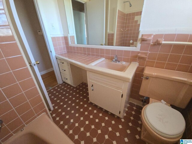 bathroom featuring tile walls, toilet, vanity, a tub, and walk in shower