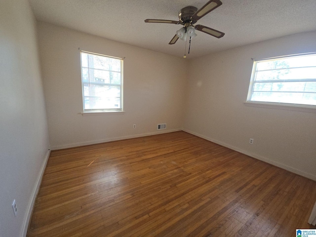 empty room with baseboards, a textured ceiling, visible vents, and wood finished floors