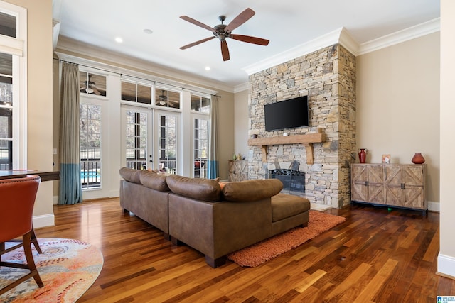 living room with a stone fireplace, crown molding, ceiling fan, and dark wood-type flooring